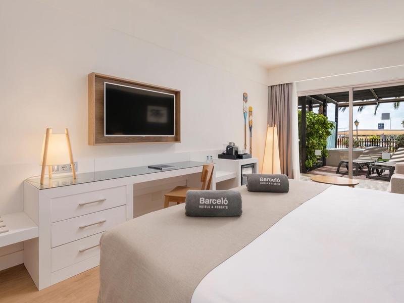 Chambre d'hôtel moderne avec lit double, télévision et terrasse avec vue sur jardin.