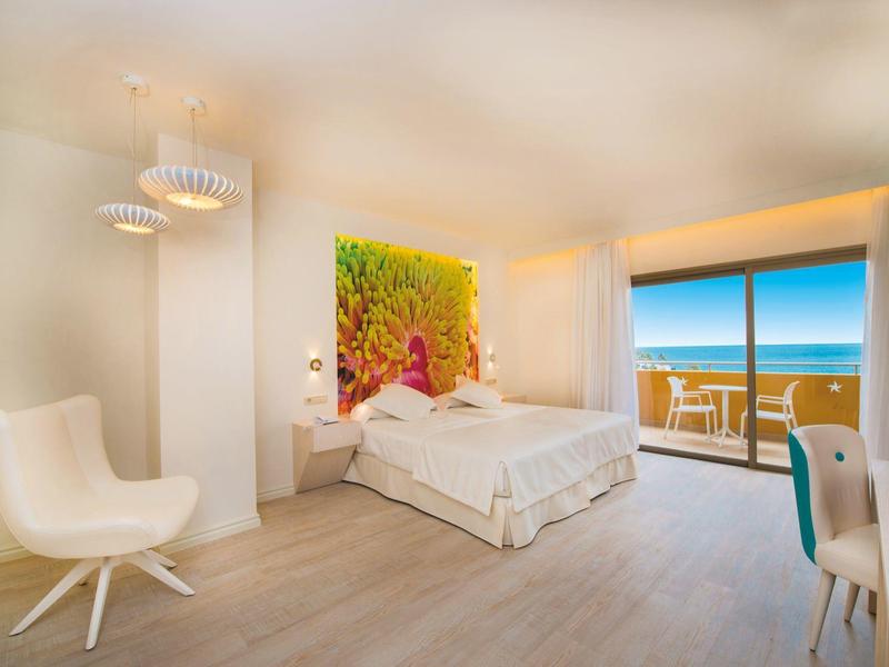 Nowoczesny pokój hotelowy z łóżkiem podwójnym, oknami sięgającymi podłogi oraz widokiem na morze.