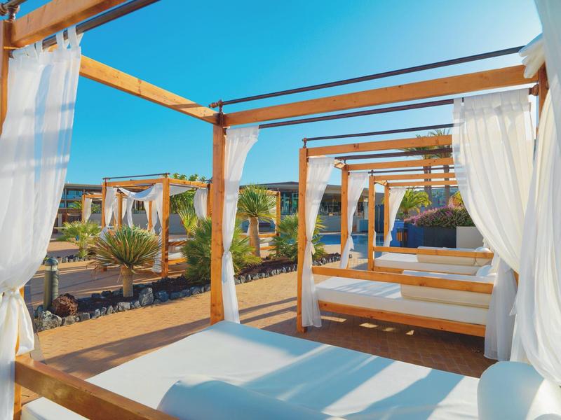 Jasne leżaki plażowe z białymi zasłonami pod czystym niebieskim niebem w hotelu.