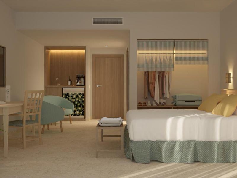 Jasny pokój hotelowy z dużym łóżkiem, miejscem do siedzenia i otwartą szafą.