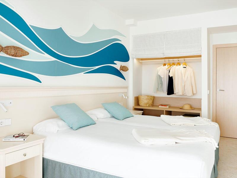 Nowoczesna sypialnia z białym łóżkiem, niebieskimi akcentami i stylizowanym wzorem fal na ścianie.