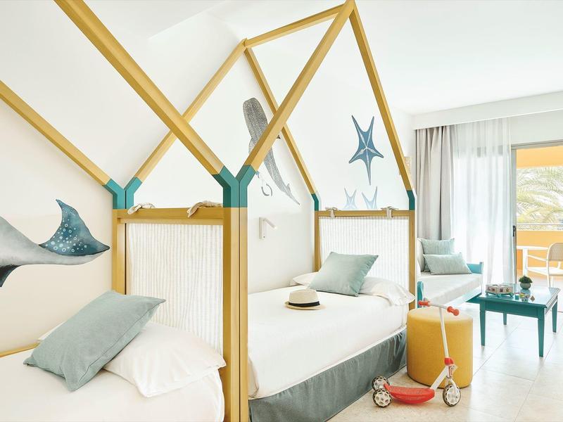 Nowoczesny pokój hotelowy z pojedynczymi łóżkami w ramkach przypominających domki z dekoracją morską.