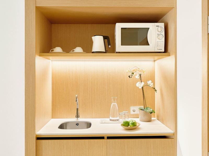 Nowoczesny aneks kuchenny z mikrofalówką, czajnikiem, zlewem i dekoracją w ciepłym drewnie.