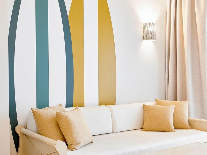 Jasny salon z białą sofą, dekoracją ścienną z desek surfingowych i beżowymi poduszkami.