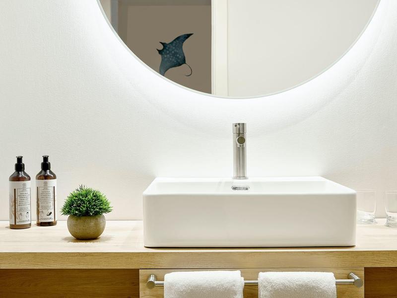 Nowoczesna umywalka z okrągłym podświetlanym lustrem i dekoracyjną rośliną w łazience.