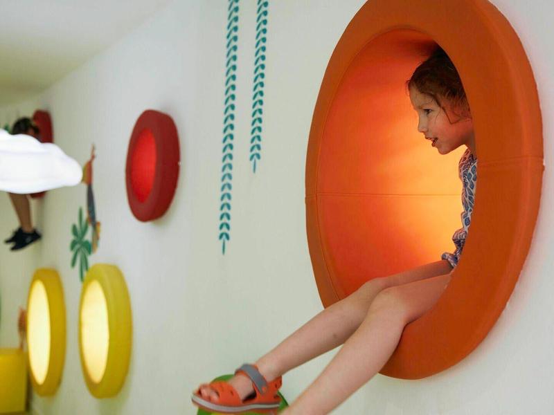 Dziecko siedzi w okrągłym, pomarańczowym otworze ściany w kolorowym, zabawnym pokoju.
