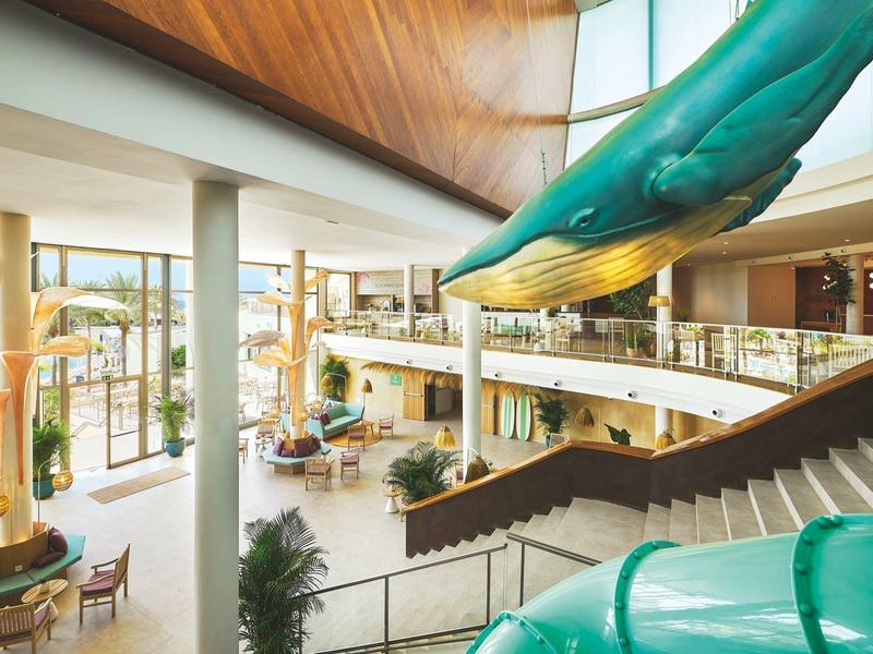 Duży hol hotelowy z schodami, miejscami do siedzenia i dużą figurą wieloryba pod sufitem.