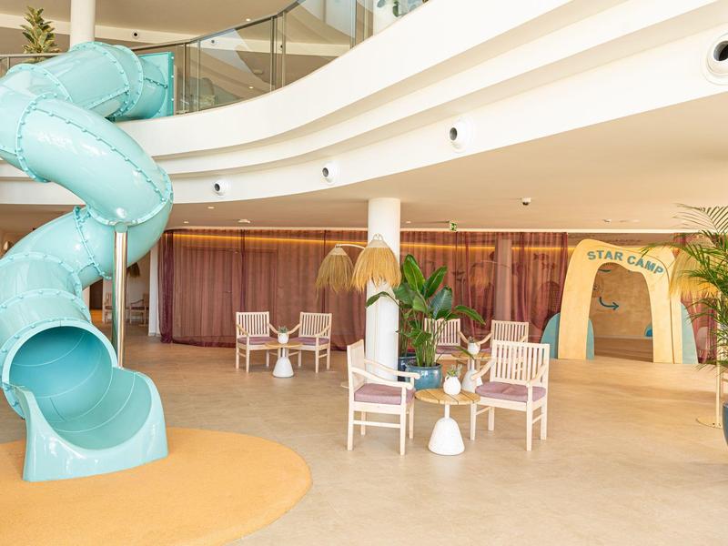 Wnętrze hotelu z niebieską zjeżdżalnią oraz kilkoma białymi stołami i krzesłami.