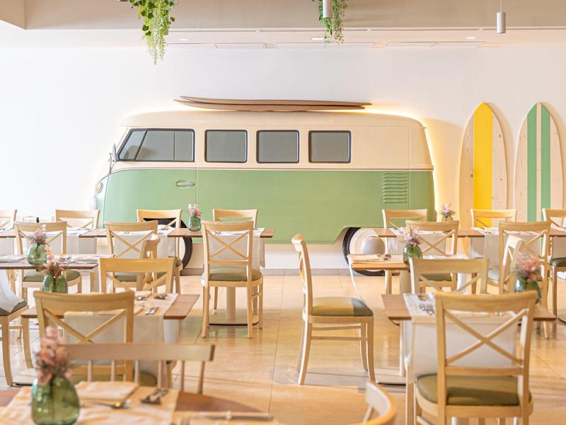 Jasna kawiarnia z drewnianymi meblami i zieloną starą dekoracją ścienną w postaci autobusu.