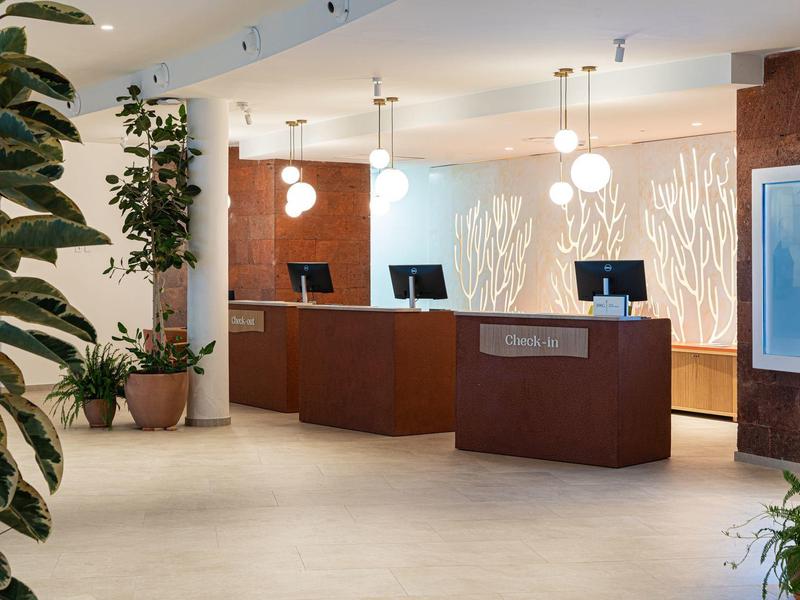 Nowoczesna recepcja hotelowa z ladami, roślinami i eleganckim oświetleniem.