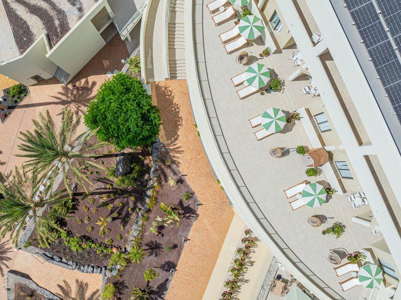 Widok z góry na taras hotelowy z parasolami i przyległym ogrodem.