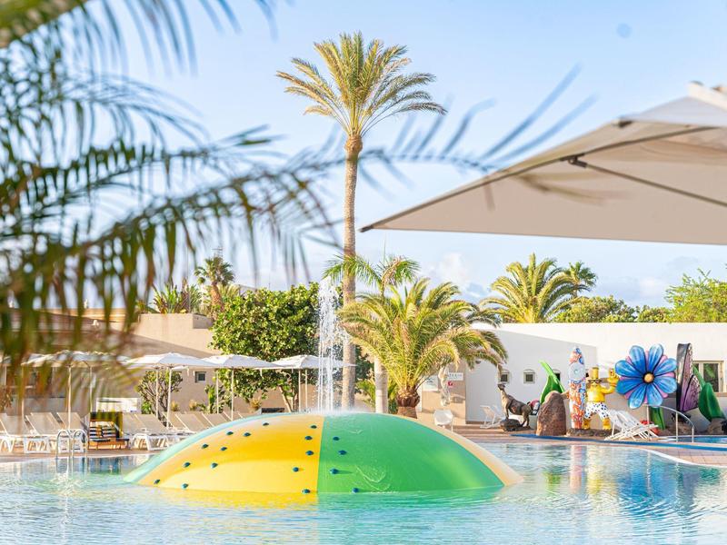 Basen z parasolem, leżakami i palmami pod niebieskim niebem w ośrodku wypoczynkowym.