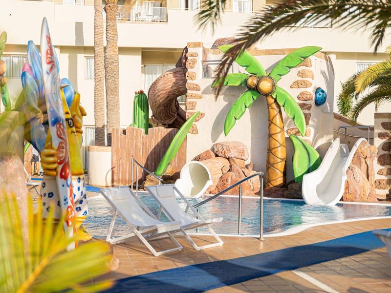 Strefa basenowa z leżakami i kolorowymi zjeżdżalniami dla dzieci w tropikalnym hotelu.