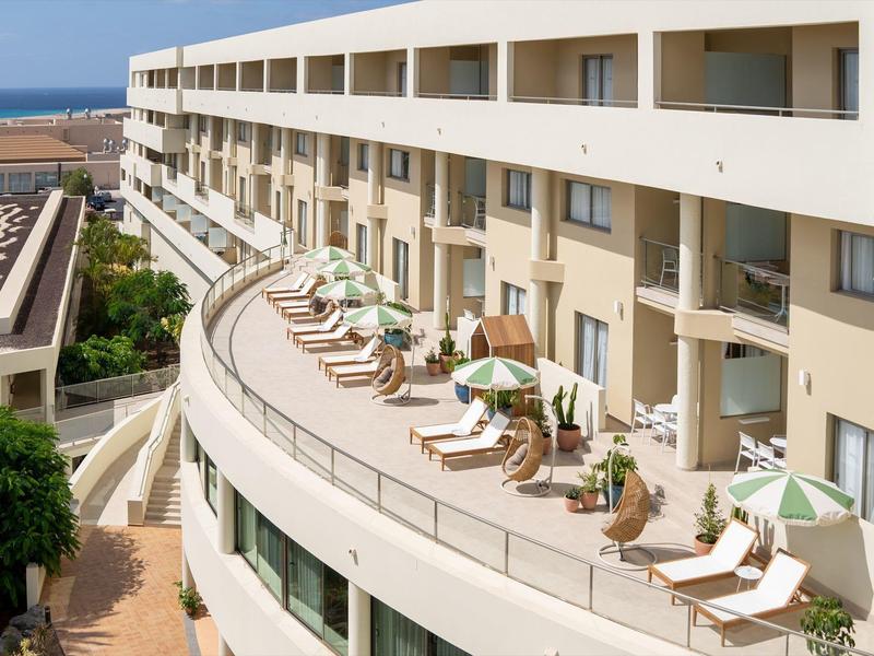 Balkon hotelowy z leżakami i zielonymi parasolami, widok na morze w tle.