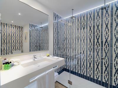Modernes Badezimmer mit weißem Waschbecken, großem Spiegel und blau-weiß gemusterter Wandfliese.
