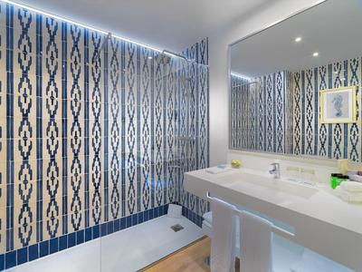 Moderner Badbereich mit blauen Rautenmustern, großer Spiegel und weißem Waschbecken mit zwei Hockern.