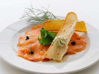 Lachs-Carpaccio mit grünem Salat, Sauce, Toastbrot und Dillzweig auf weißem Teller.