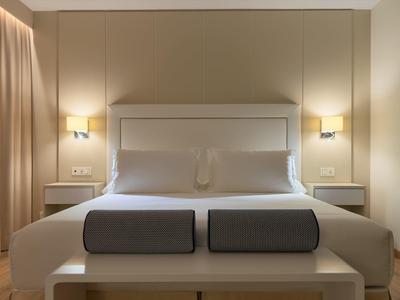 Modernes Schlafzimmer mit großem Bett, grauen Kissen, Nachttischen und warmem Wandlicht.