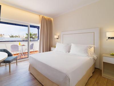 Brightly furnished hotel room with double bed, balcony, and view of palm trees.