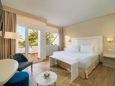 Bright hotel room with double bed, balcony, and modern wooden floor furnishings.