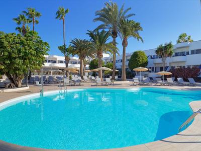 Large round pool with clear water, surrounded by palm trees and lounge chairs under a blue sky.