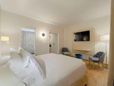 Modern hotel room with large bed, two chairs, and wall-mounted flat-screen TV.