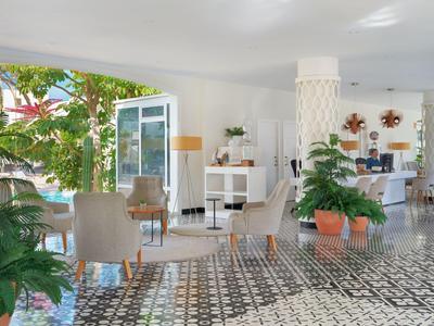 Bright hotel lobby area with plants, seating, and patterned floor tiles.