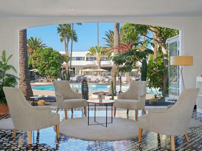Bright seating area with four chairs and table in front of pool with palm trees at hotel.