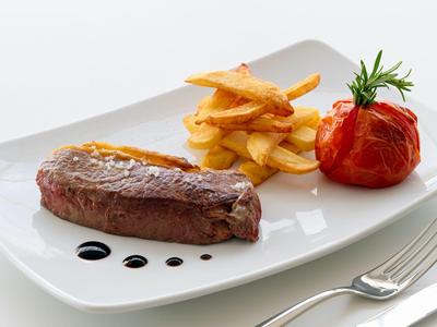Juicy steak with fries and a baked tomato on a white plate.