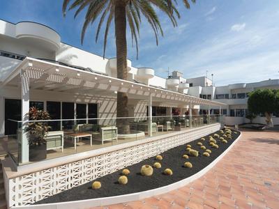 Modern hotel exterior with terrace, tables, and chairs under a white pergola.