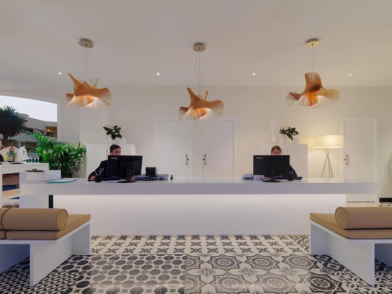 Moderna recepción con mostrador blanco, bancos y iluminación decorativa.