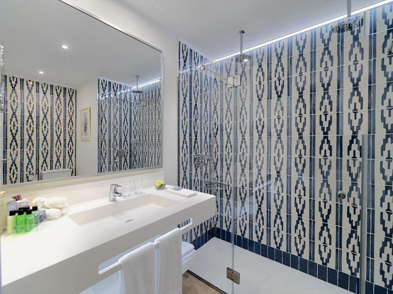 Baño moderno con gran espejo, lavabo y pared de ducha con patrón en azul y blanco.