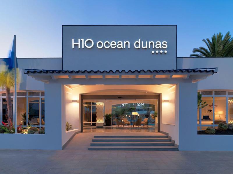 Entrada iluminada del hotel H10 Ocean Dunas con piscina al atardecer.
