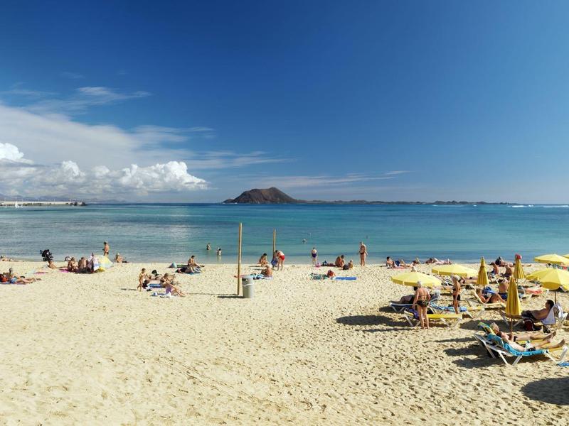 Amplia playa de arena con sombrillas y gente frente al mar y cielo azul claro.