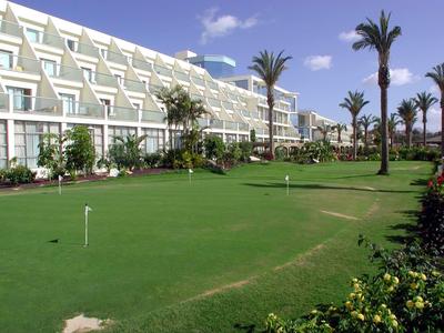 Ampio complesso alberghiero con area pratica golf curata e palme sotto il cielo azzurro.