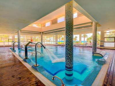 Piscina coperta moderna con giochi d'acqua e pavimento in legno in un edificio luminoso.