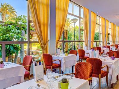 Sala da pranzo dell'hotel luminosa con tavoli apparecchiati di bianco e vista sul giardino