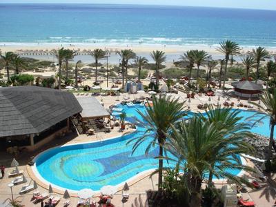 Vista di una piscina di resort con palme e una spiaggia sullo sfondo.