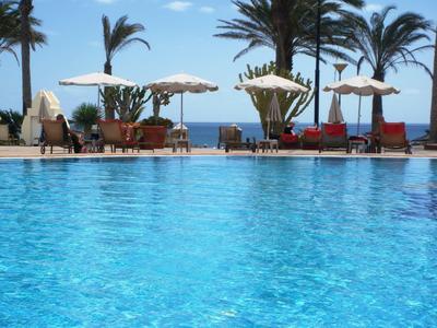 Acqua chiara e blu della piscina con ombrelloni, palme e vista sul mare.