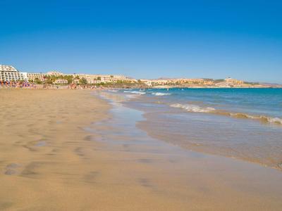 Ampia spiaggia di sabbia con onde dolci e edifici di hotel sullo sfondo sotto un cielo limpido.
