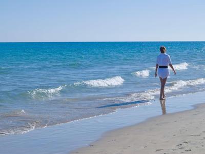 Una persona cammina lungo la spiaggia soleggiata mentre le onde lambiscono dolcemente la riva.