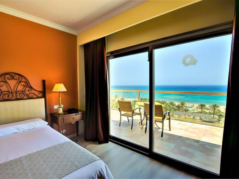 Camera d'albergo accogliente con vista mare attraverso grandi porte scorrevoli in vetro e mobili da balcone.