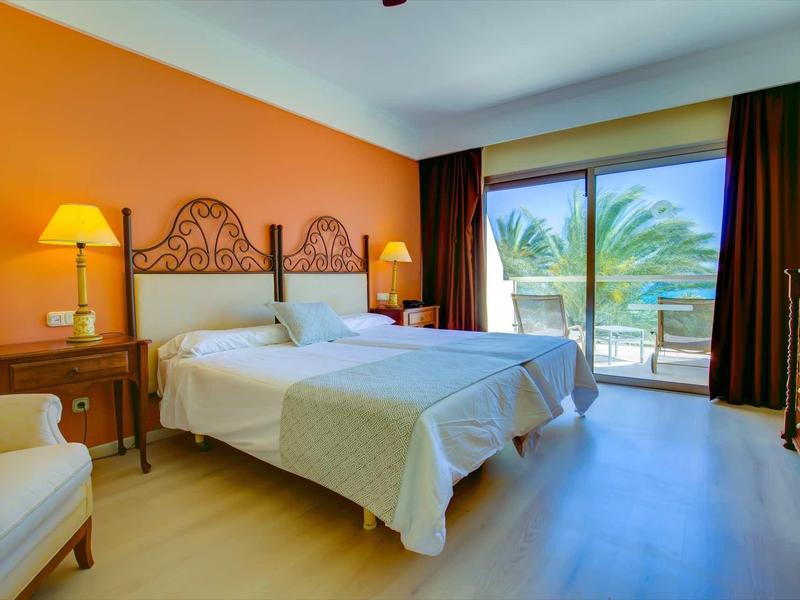 Camera d'hotel con due letti singoli, parete arancione, vista balcone e pavimento in legno.