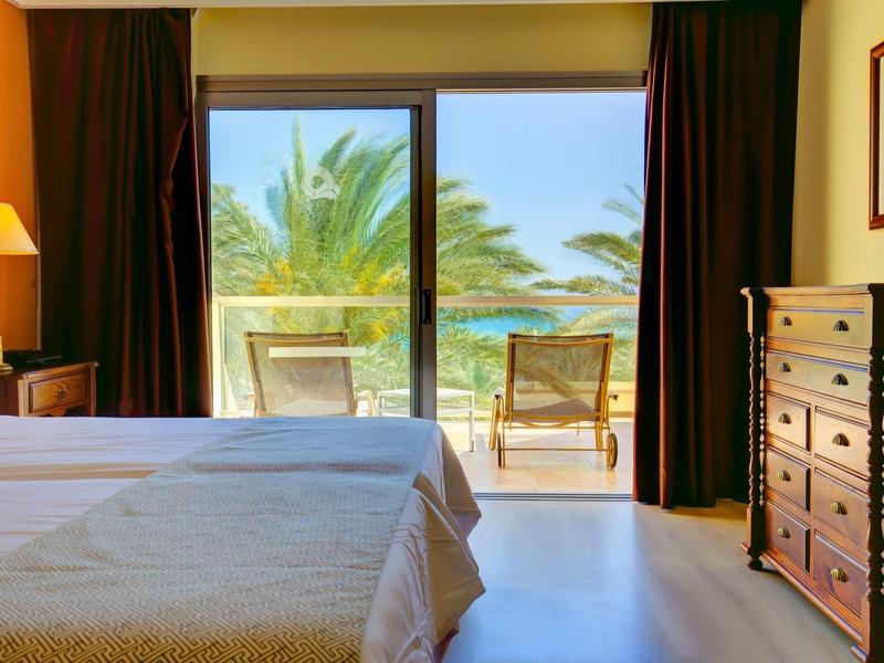 Camera d'albergo con due letti e vista su una terrazza con sedie e palme.