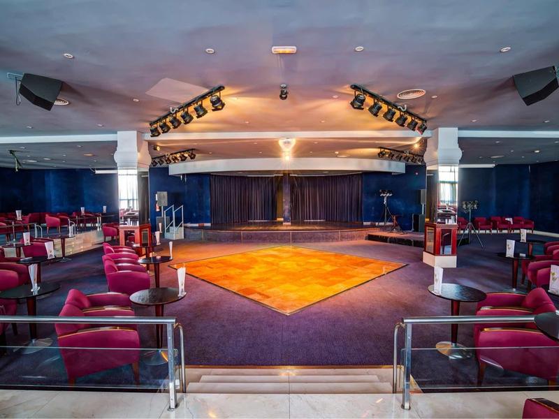 Ampio spazio per eventi elegante con palco, poltrone rosse e illuminazione a soffitto.