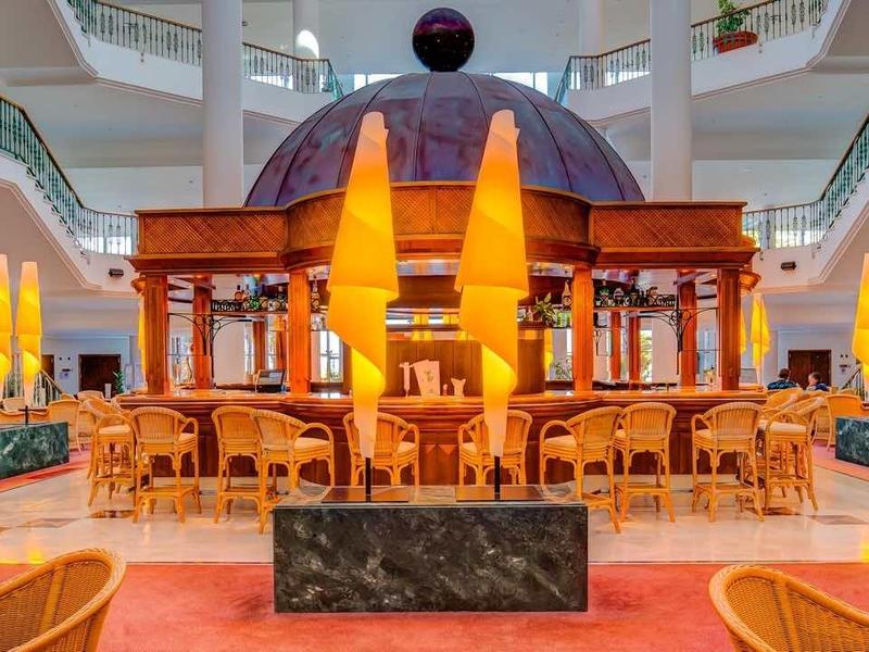 Ampia e luminosa hall dell'hotel con un chiosco centrale in legno e aree salotto accoglienti.