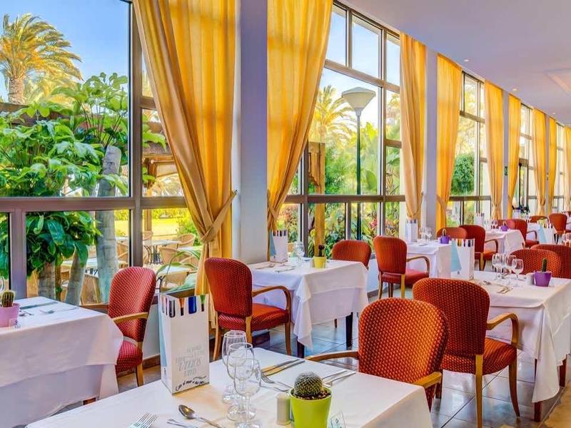 Sala da pranzo dell'hotel luminosa con tavoli apparecchiati di bianco e vista sul giardino