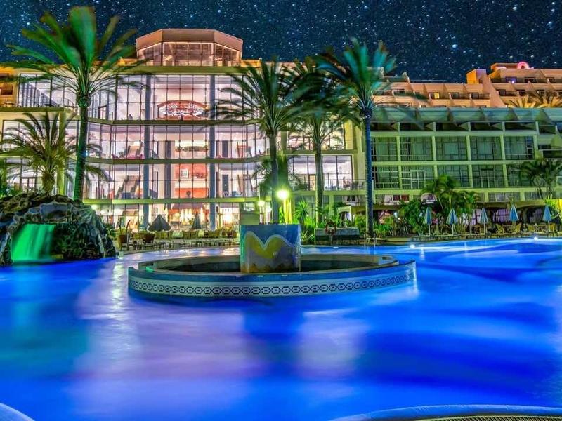 Hotel con piscina illuminata e palme di notte sotto un cielo stellato