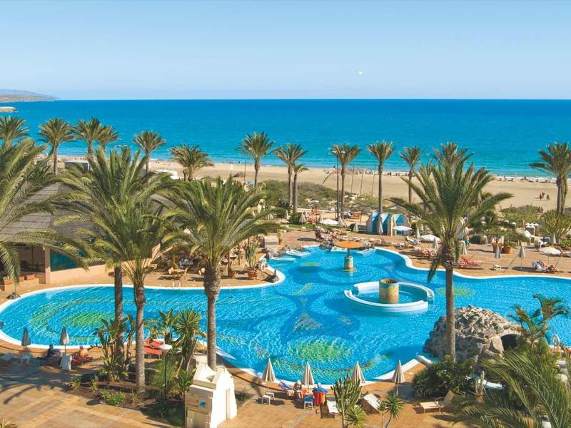 Grande piscina del resort con palme e vista mare sulla spiaggia.