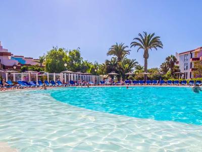 Velký hotelový bazén s čistou vodou, obklopený lehátky a tropickou vegetací.